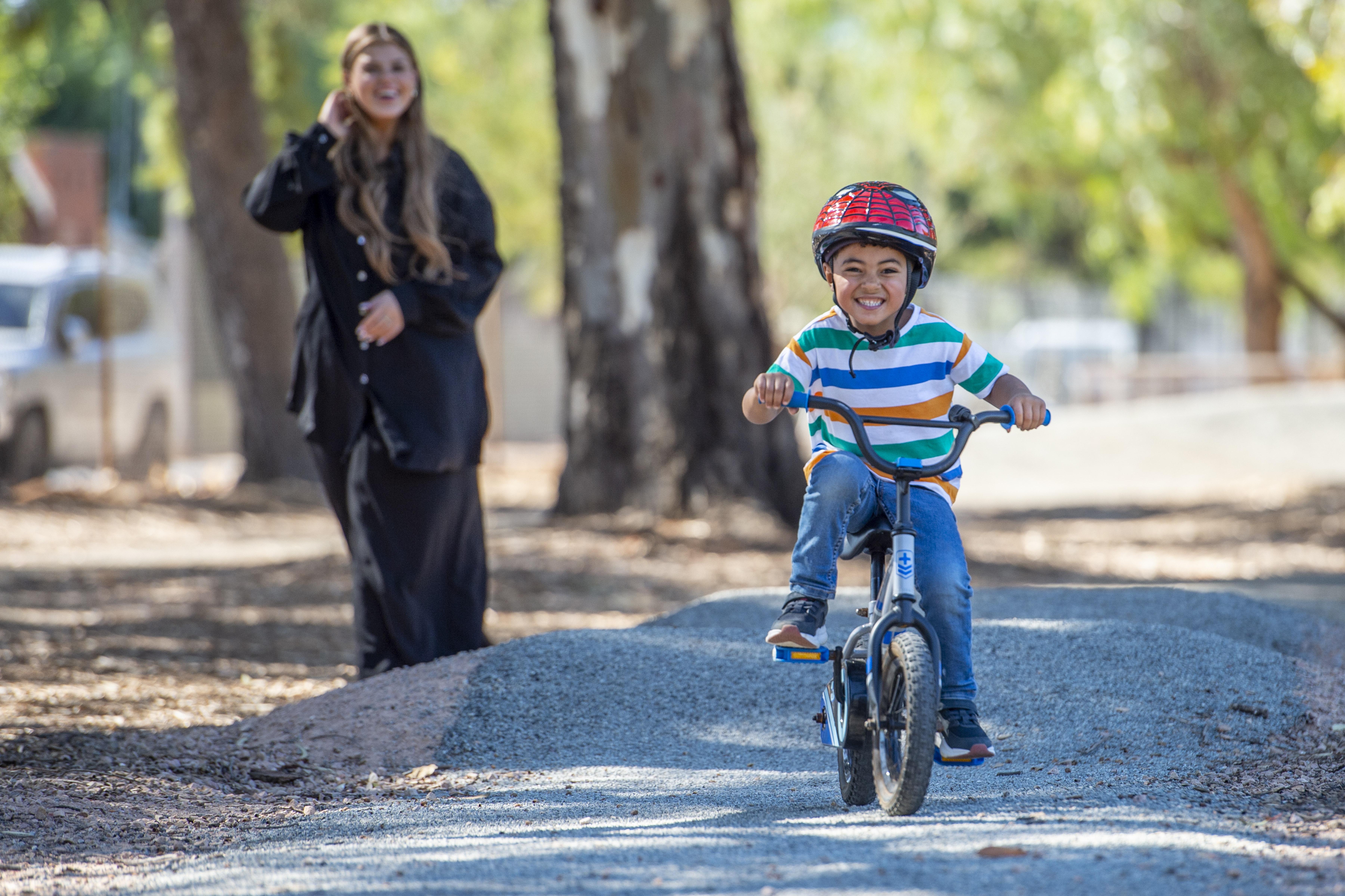 child riding bike on pump track with mother in background smiling
